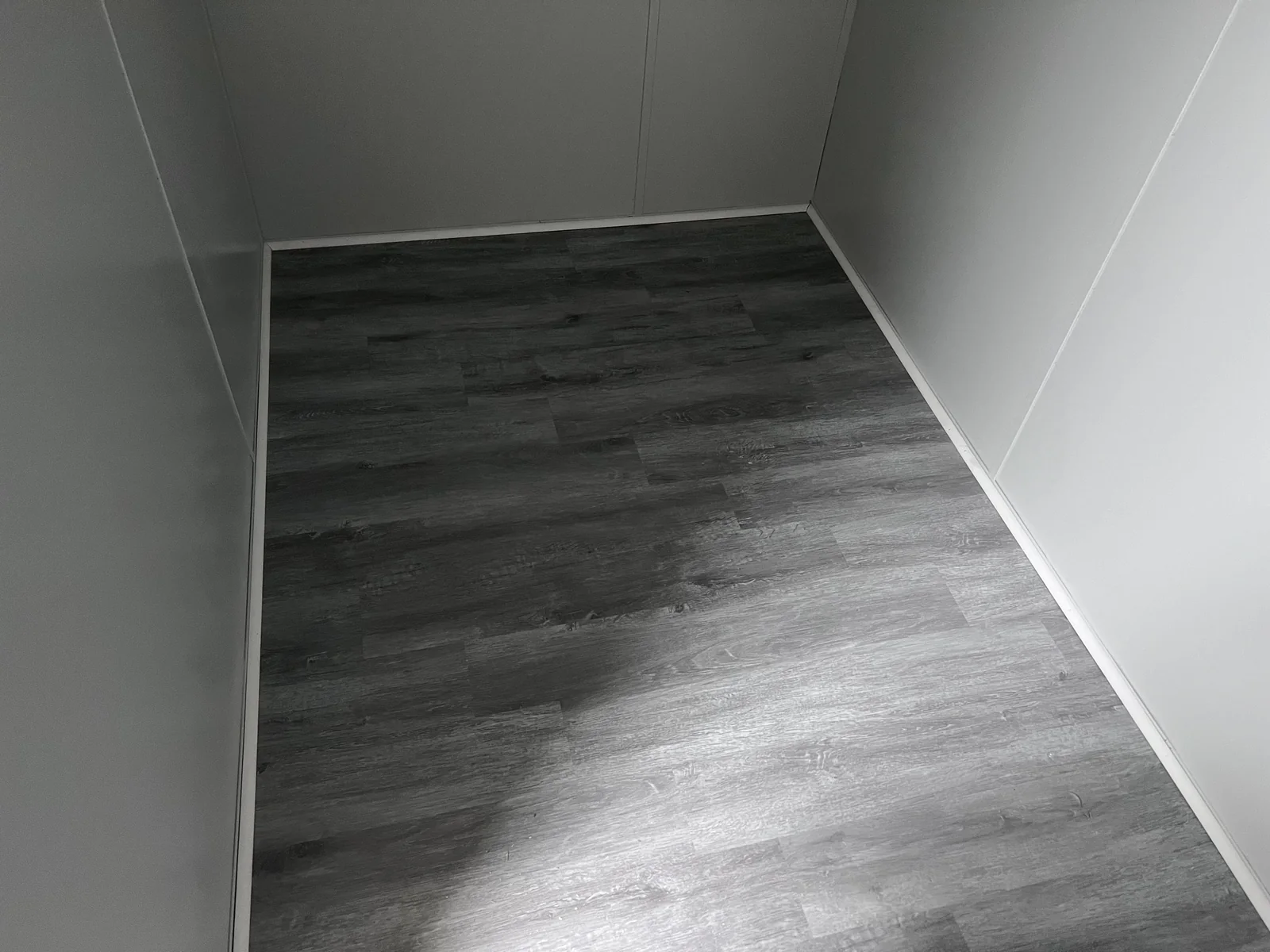 Grey wood-look flooring in a small room with light walls and white baseboards